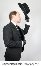 Portrait Of British Butler In Dark Suit And Leather Gloves Doffing Bowler Hat In Polite Greeting. Vintage Style Of Elegant English Gentleman.