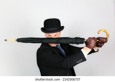 Portrait Of British Man In Dark Suit And Bowler Hat Holding Umbrella In Action Pose. Film Noir Secret Agent Spy Hero Concept.