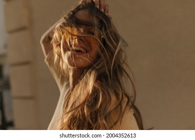 Portrait of brown-haired lady having fun ruffling her hair close-up against brown wall. On face are translucent yellow round glasses.