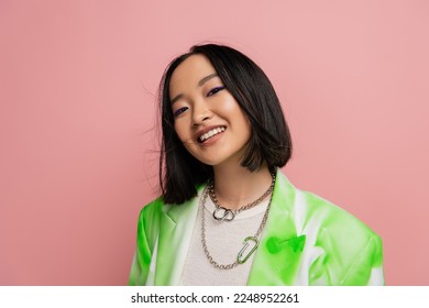 portrait of brunette asian woman in trendy outfit and makeup looking at camera isolated on pink Arkivfotografi