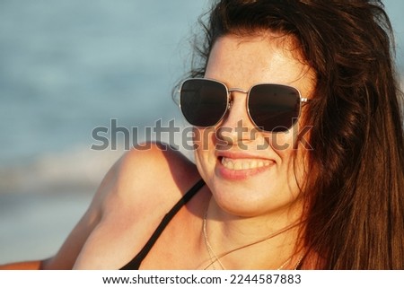 Portrait of brunette in black glasses on the beach at sunrise. Happy woman on the summer beach. Portrait of young smiling pretty girl. 