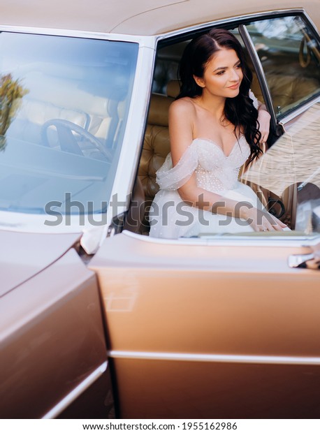 Portrait of brunette bride sitting in\
the front seat of a pink retro car. Concept of\
bride