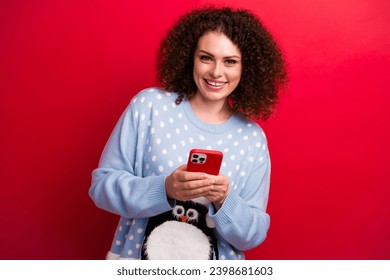 Portrait of brunette curls hair girl in penguin sweater using smartphone for eshopping christmas gifts isolated on red color background - Powered by Shutterstock