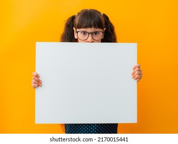 Portrait Of A Brunette Girl Child With Glasses Schoolgirl Girl Child Kid Pointing Finger On White Poster Banner Isolated On Yellow Color Background, Advertising, Billboard, Mockup