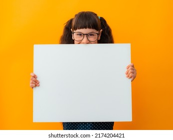 Portrait Of A Brunette Girl Child With Glasses Schoolgirl Girl Child Kid Pointing Finger On White Poster Banner Isolated On Yellow Color Background, Advertising, Billboard, Mockup