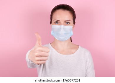 Portrait of a brunette girl in a medical mask, thumb up gesture. Isolated on pink background. - Shutterstock ID 1765677251