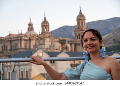 portrait of a brunette latina girl, dressed in blue, with the cathedral of jaén in a blurred background