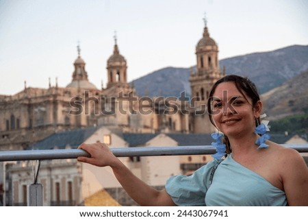 portrait of a brunette latina girl, dressed in blue, with the cathedral of jaén in a blurred background