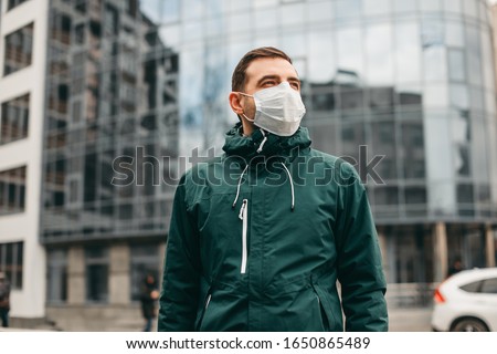 portrait of brunette man in a surgical bandage on a background of a modern building, coronavirus, illness, infection, quarantine, medical mask