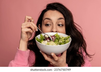Portrait of a brunette pricking with a fork a portion of vegetable salad in the bowl during the studio photo shoot