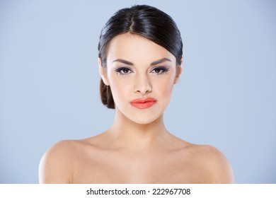 Portrait Of Brunette Woman With Bare Shoulders And Hair Pulled Back Against Blue Background