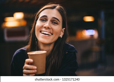 Portrait of brunette woman drinking hot coffee cup with milk froth mustache in coffee shop. She is smiling and on her lips foam.  Copy space for text