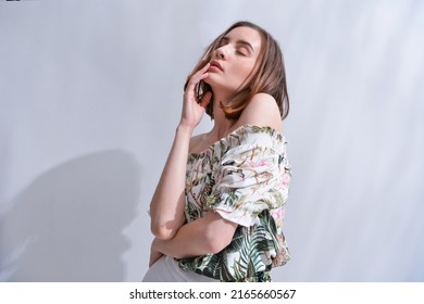 Portrait Of A Brunette Young Woman In Summer Floral Pattern Print. Shirt,with White Pants,posing In Studio

