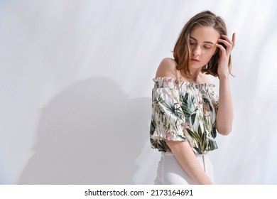 Portrait Of A Brunette Young Woman In Summer Floral Pattern Print. Shirt,with White Pants,posing In Studio

