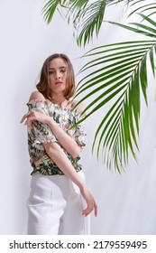 Portrait Of A Brunette Young Woman In Summer Floral Pattern Print. Shirt,with White Pants With Green Palm 