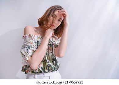 Portrait Of A Brunette Young Woman In Summer Floral Pattern Print. Shirt,with White Pants With Palm Shadow