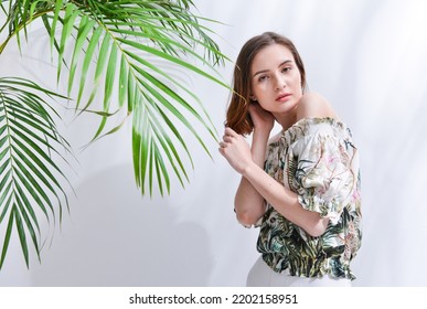 Portrait Of A Brunette Young Woman In Summer Floral Pattern Print. Shirt,with White Pants,with Green Palm 