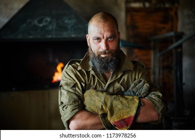 Portrait of a brutal, confident blacksmith, a man with a beard. Standing in the workshop, folding his arms over his chest - Powered by Shutterstock