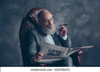 Portrait Of Brutal Harsh Old Man In Tuxedo Holding, Reading, Looking At Newspaper, Smoking Cigar, Sitting In Leather Armchair, Shares, Money, Stock, Economy, Finance, Gray Background