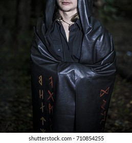 Portrait Of A Brutal Man In A Black Robe. Satanist Wear Dark Shroud With Bloody Runes Against Night Forest. 