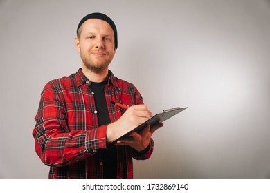 Portrait Of A Brutal Successful Builder, On A Light Background. Average Plan Of A Man In A Plaid Work Shirt.Isolation, Copy Space Next To A Person.