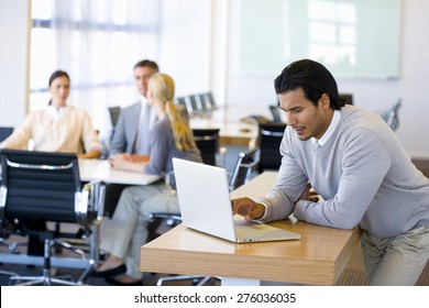 Portrait Of Business Executive Using Laptop With People Meeting In The Background.