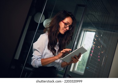 Portrait Of A Business Lady In The Office From The Side Looking At The Tablet. Dark Background.