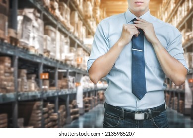 Portrait Of Business Man Standing In Warehouse Distribution With Dressing Up And Adjusting Tie On Neck, Dark Low Light Warehouse In The Background.