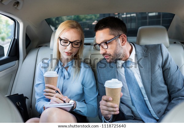 portrait of business people with coffee to\
go working on project on back seats in\
car