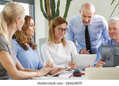 Portrait of business people discussing in a meeting while sitting at conference desk and using laptop and digital tablet.