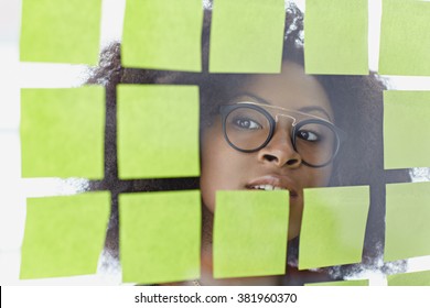 Portrait einer Geschäftsfrau mit einem afro hinter klebrigen Noten in einem hellen Glasbüro
