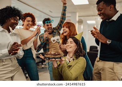 Portrait of a business woman who uses a wheelchair celebrating birthday and having a party with multiracial colleagues in an office. Happy businesswoman with disability blowing candles on a cake. - Powered by Shutterstock