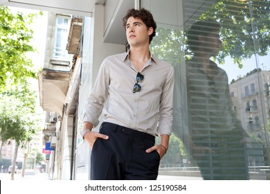 Portrait of a businessman leaning on an office buildings glass window in the city with his hands in his pockets, waiting.