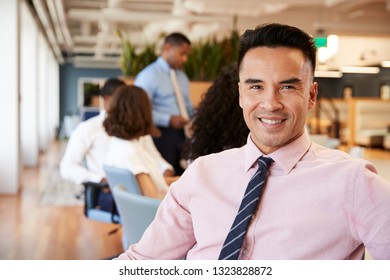 Portrait Of Businessman In Modern Office With Colleagues Meeting Around Table In Background