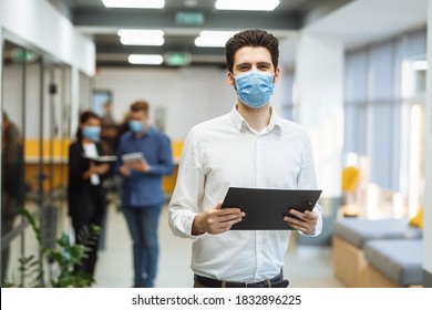 Portrait of a businessman at the office in a mask. A group of collegues discuss business matters at the corridor wearing medical masks to protect from coronavirus desease during global pandemic. - Powered by Shutterstock