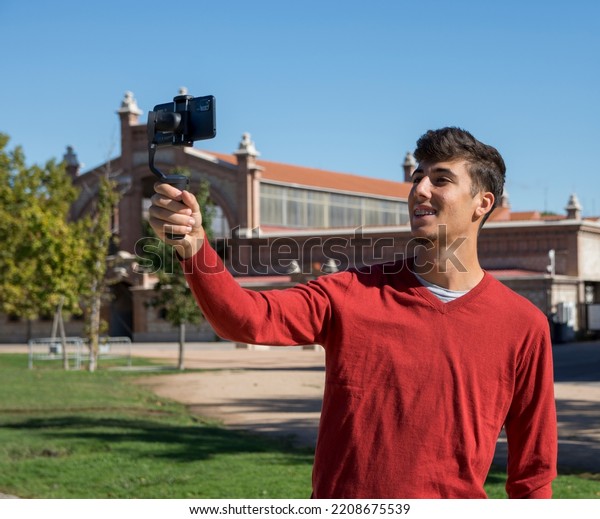Portrait of businessman recording video presentation at\
smartphone with steadycam. Focused young man standing outside,\
holding steadycam while recording video presentation about new\
object 