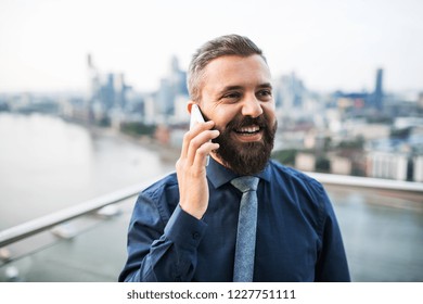 A portrait of businessman with smartphone standing against London view panorama.