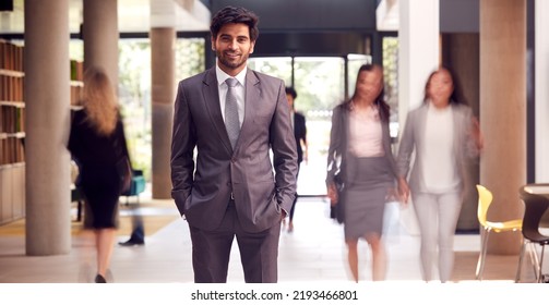 Portrait Of Businessman Standing In Lobby Of Busy Modern Office Building