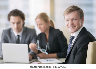 Portrait of businessman with subordinates at the background. Group of business people, friendly smiling middle aged man looking at camera, teamwork concept, conference hall for rent, applicant for job