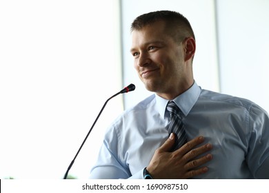Portrait of businessman in suit standing on podium speaking at conference in room. Attractive man reporting for audience on stage. Business and public talk concept