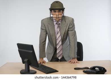 Portrait of a businessman wearing a cricket helmet and using a computer