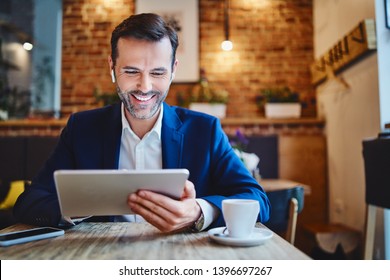 Portrait of businessman with wireless headphones using tablet in cafe - Powered by Shutterstock