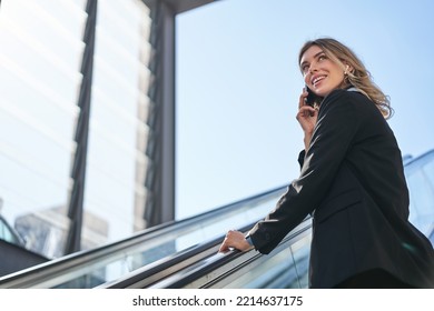 Portrait of businesswoman in black suit, going up on escalator, talking on mobile phone. Saleswoman walking in city, having a call - Powered by Shutterstock