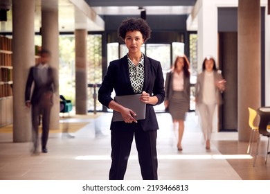 Portrait Of Businesswoman With Digital Tablet Standing In Lobby Of Busy Modern Office Building