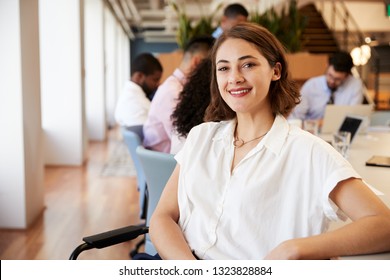 Portrait Of Businesswoman In Modern Office With Colleagues Meeting Around Table In Background