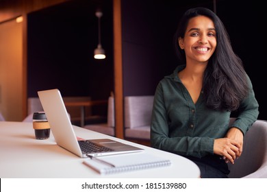 Portrait Of Businesswoman Sitting At Meeting Table Working On Laptop In Modern Open Plan Office