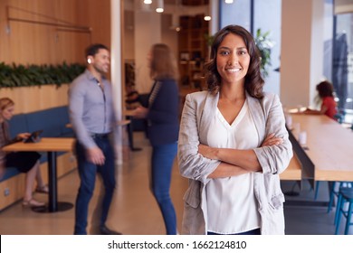 Portrait Of Businesswoman Standing In Busy Modern Open Plan Office  With Colleagues In Background