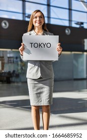 Portrait Of Businesswoman Standing While Holding White Board With TOKYO Signage In Arrival Area At Airport