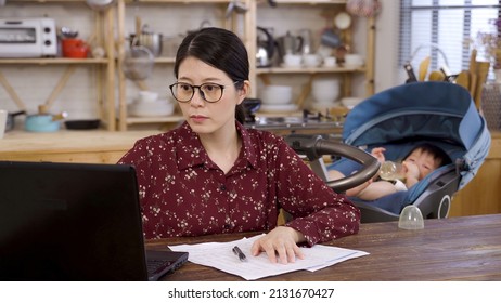 Portrait Businesswoman Is Turning To Check On Her Child Who’s Drinking Milk From Bottle In The Stroller While Doing Paperwork With A Laptop In The Dining Room.