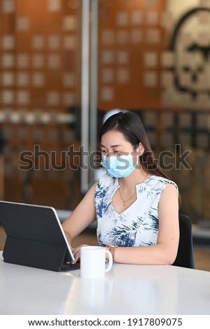 Portrait of businesswoman wearing protective mask working on her project with computer tablet at modern office.